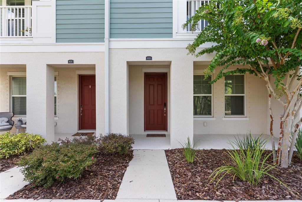The exterior of a two-story townhouse features beige stucco walls, two red front doors, and landscaping — 9533 CAVENDISH DRIVE, TAMPA, FL