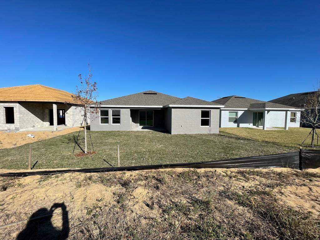The rear exterior of a gray single-story house with a lawn and neighboring construction — 1186 TUPELO TRAIL, HAINES CITY, FL