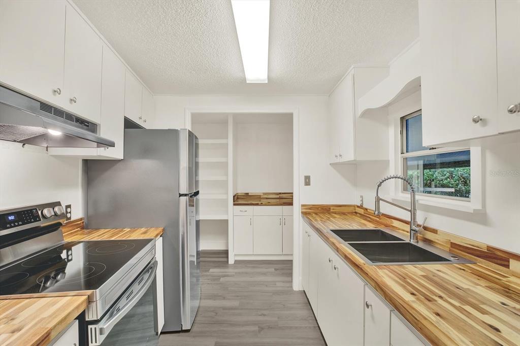 A kitchen features white cabinets, butcher block countertops, stainless steel appliances, and gray flooring — 10051 HUNTLEY STREET, NEW PORT RICHEY, FL