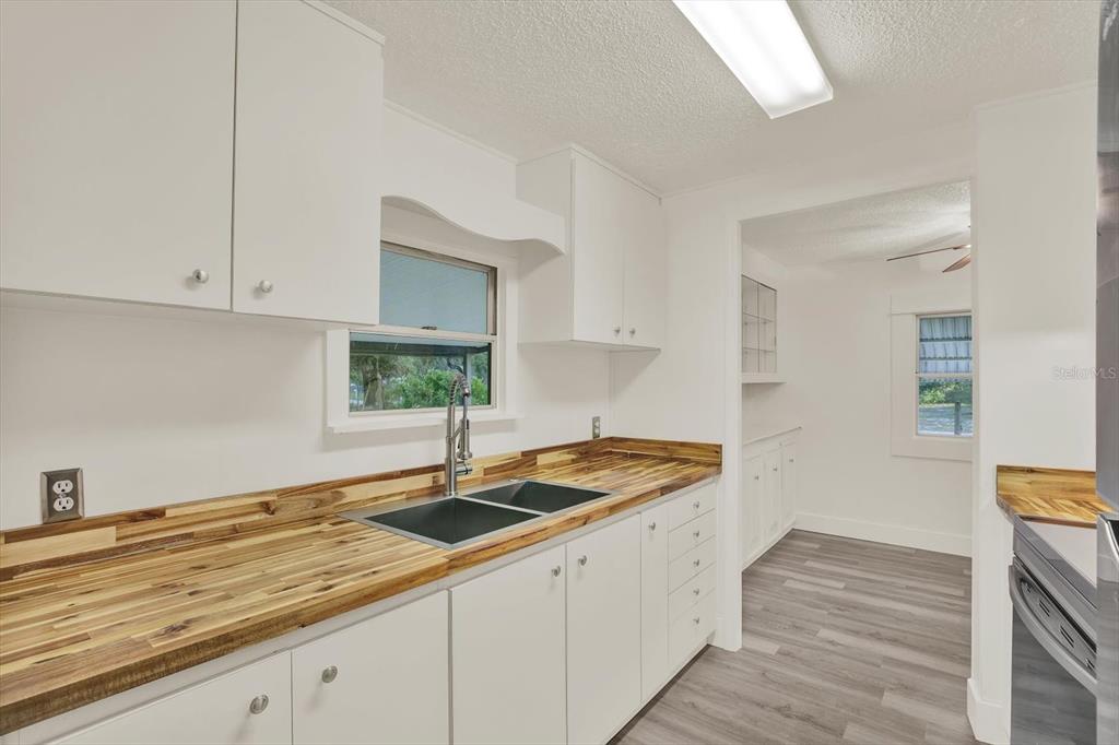 A kitchen features white cabinets, a wood countertop, a double sink, and gray flooring — 10051 HUNTLEY STREET, NEW PORT RICHEY, FL