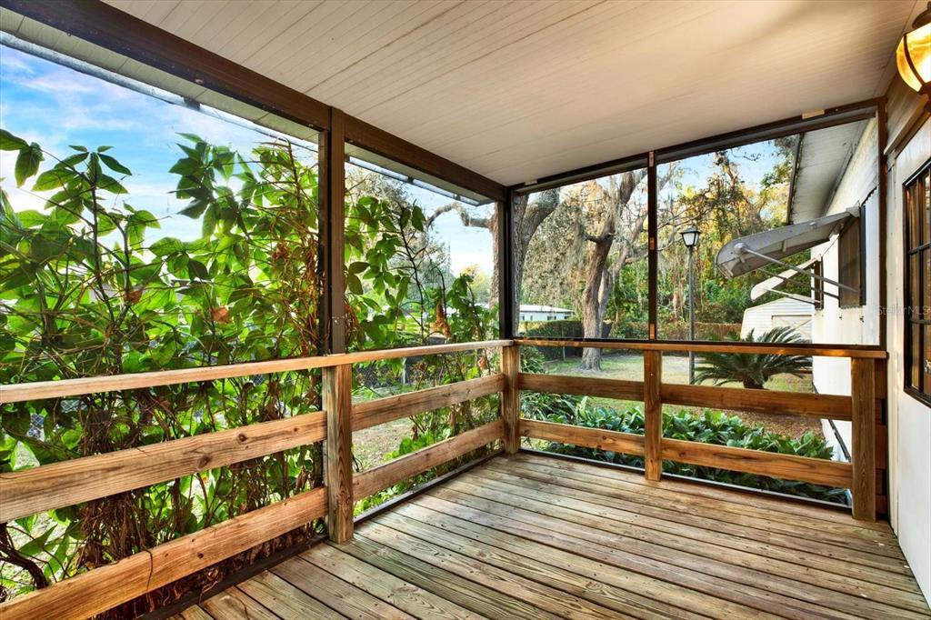 A screened-in wooden porch features a deck floor, wooden railings, and views of a backyard — 10051 HUNTLEY STREET, NEW PORT RICHEY, FL