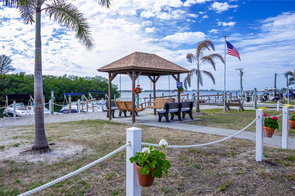 A wooden gazebo with swings sits near a boat dock under a blue sky — 10315 CORTEZ ROAD W UNIT 2-4, BRADENTON, FL
