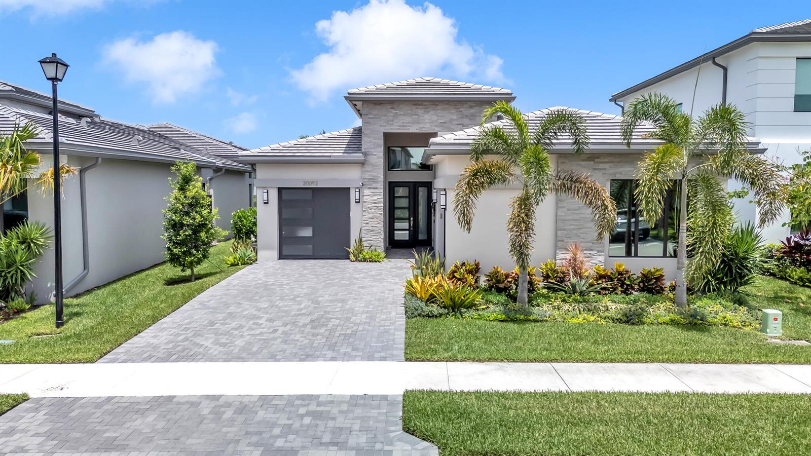A modern single-story house with a stone facade, gray tile roof, and a paved driveway — 20092 Hirono Lane, Boca Raton FL 33434, BOCA RATON, FL