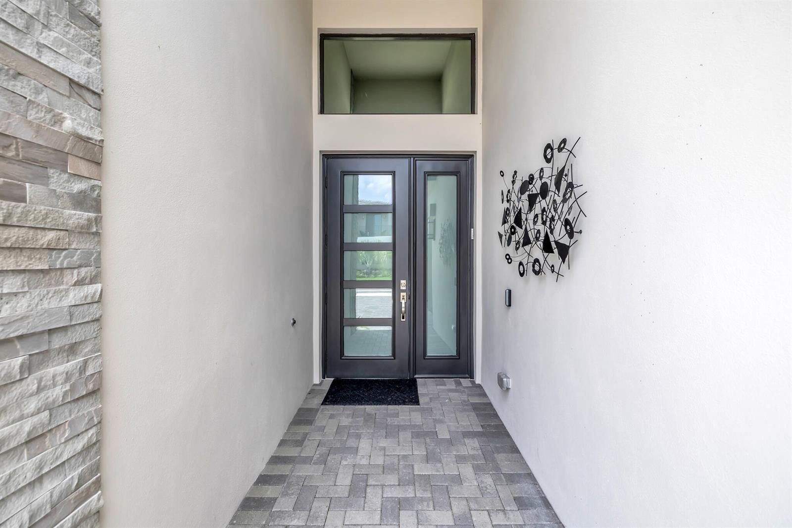 A modern entryway features a dark double door with glass panels and stone siding — 20092 Hirono Lane, Boca Raton FL 33434, BOCA RATON, FL