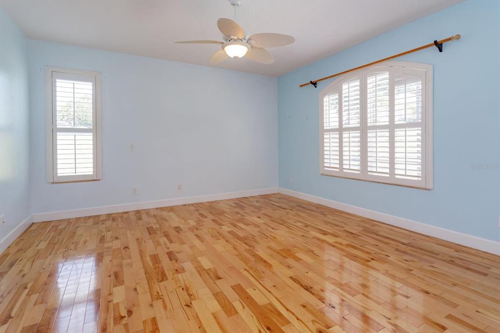 An empty bedroom features light blue walls, hardwood flooring, a ceiling fan, and two windows — 12560 KATHERINE CIRCLE, CLERMONT, FL
