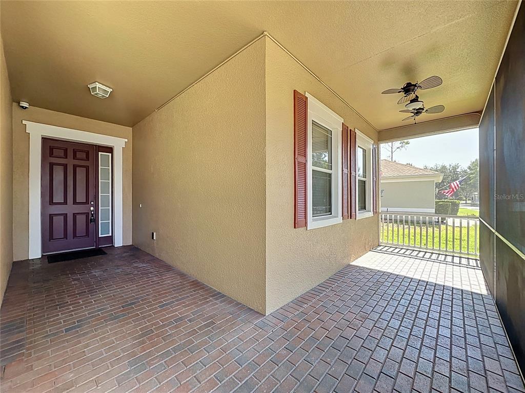 A covered brick porch features a dark front door, shuttered windows, and a ceiling fan — 157 CREPE MYRTLE DRIVE, GROVELAND, FL