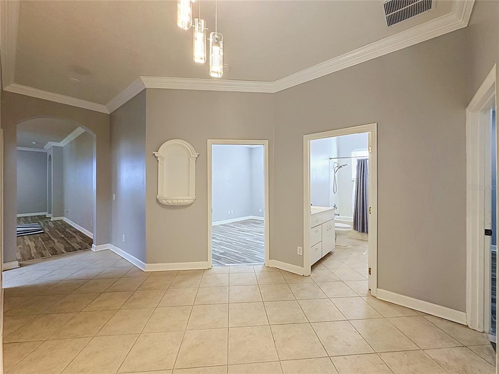 A tiled foyer leads to a bedroom and a bathroom with gray walls and crown molding — 157 CREPE MYRTLE DRIVE, GROVELAND, FL