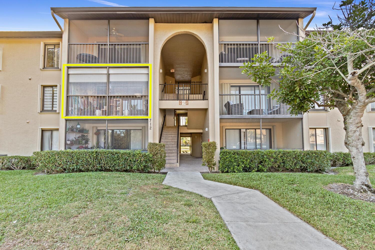 A three-story apartment building exterior features a highlighted second-floor balcony with a partial privacy screen — 712 Sunny Pine Way # E2, FL 33415, FL