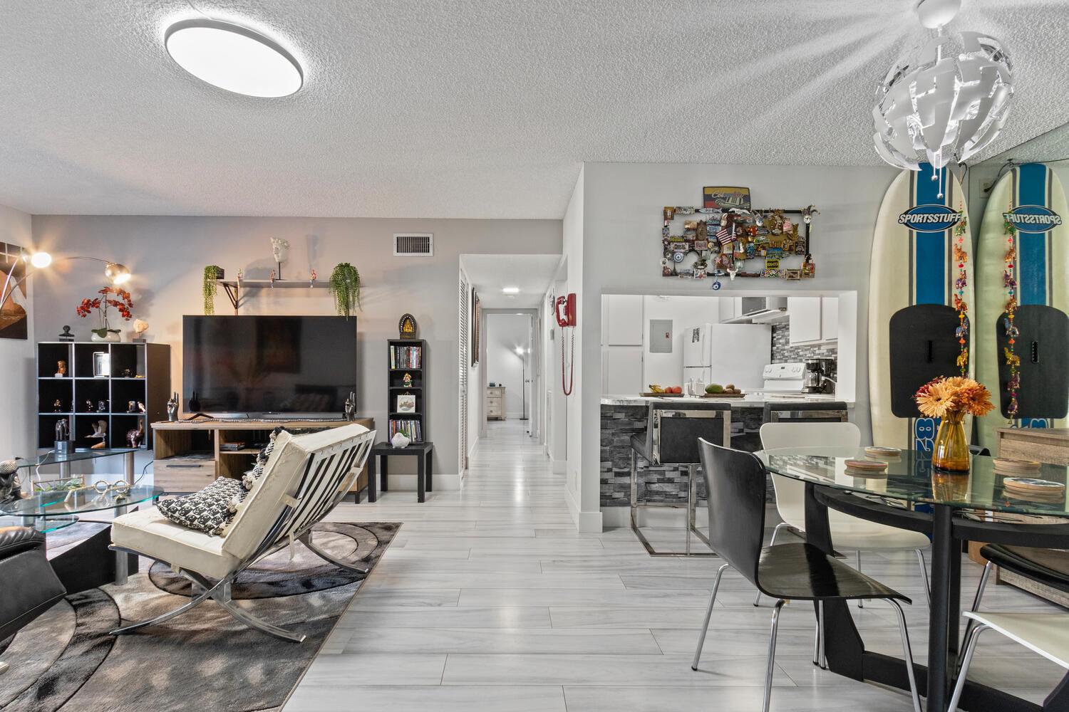 An open-concept living and dining area features light wood-look flooring, a kitchen pass-through, and surfboards — 712 Sunny Pine Way # E2, FL 33415, FL