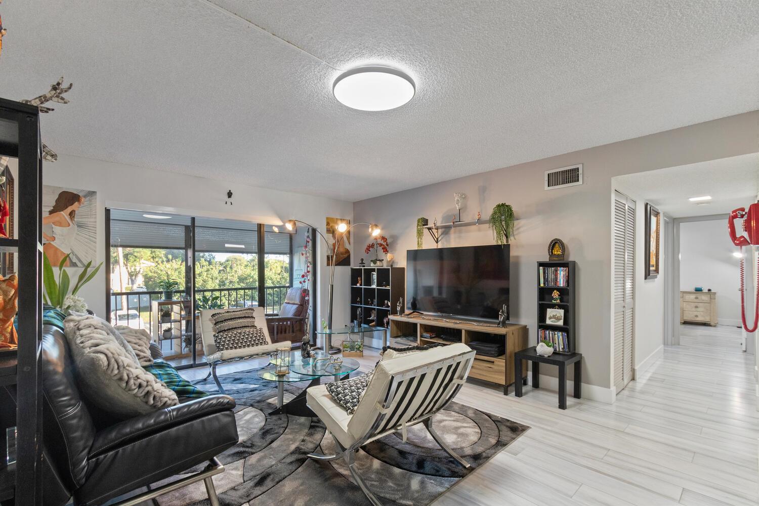 A living room features a black leather sofa, two white accent chairs, and a television — 712 Sunny Pine Way # E2, FL 33415, FL