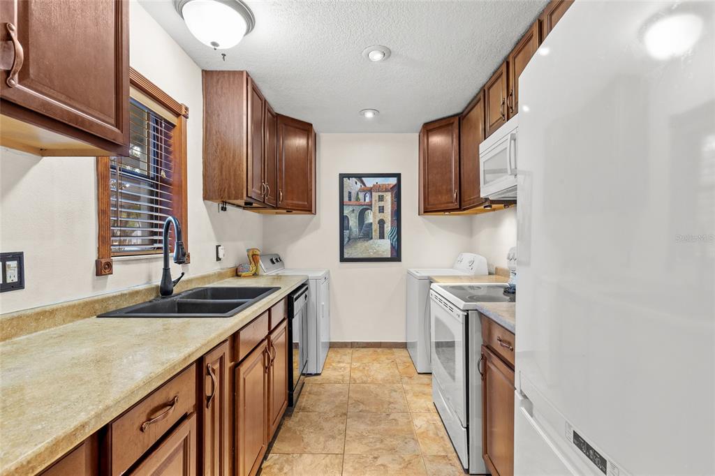 A galley-style kitchen features wood cabinets, tan countertops, a black sink, and white appliances — 4340 AQUA VISTA DRIVE UNIT A, ORLANDO, FL