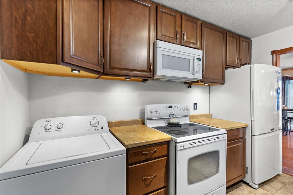 A kitchen features dark wood cabinets, a white stove, a microwave, and a laundry machine — 4340 AQUA VISTA DRIVE UNIT A, ORLANDO, FL