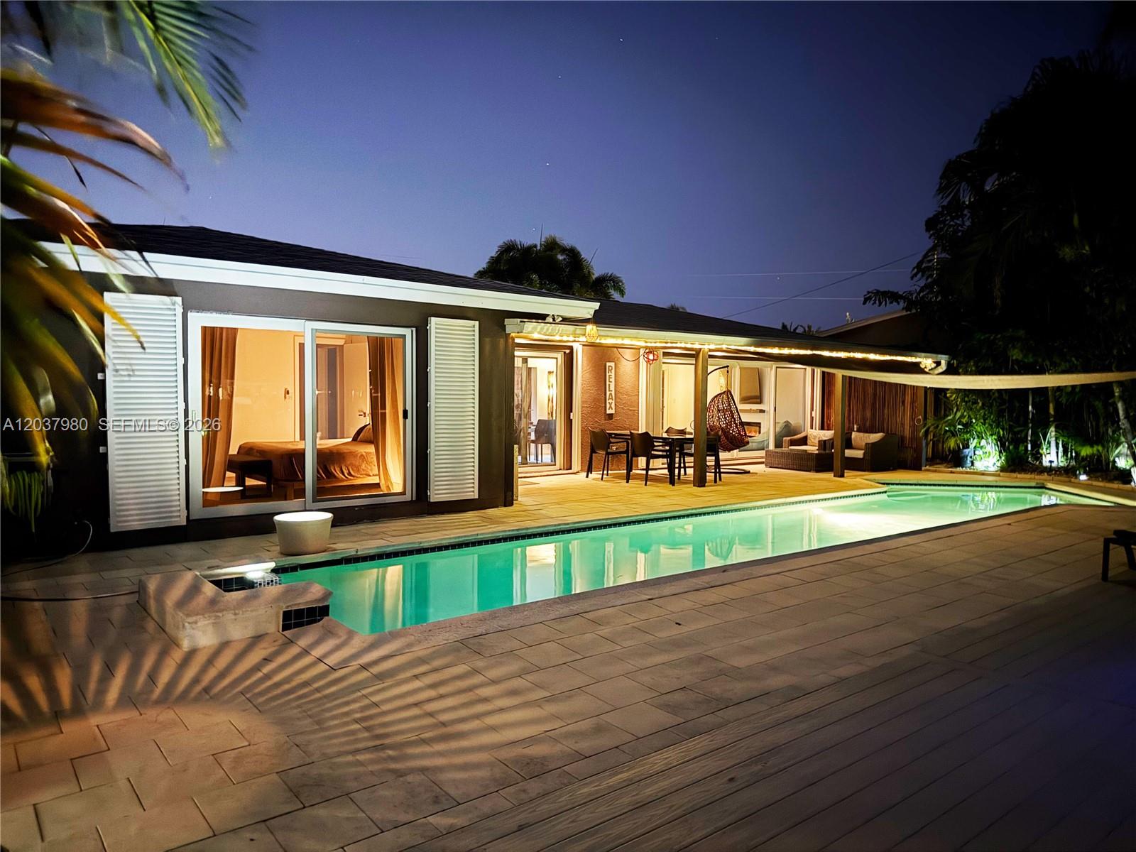A backyard swimming pool sits in front of a house with a covered patio at night — 2100 NE 24th St, Wilton Manors FL 33305, WILTON MANORS, FL