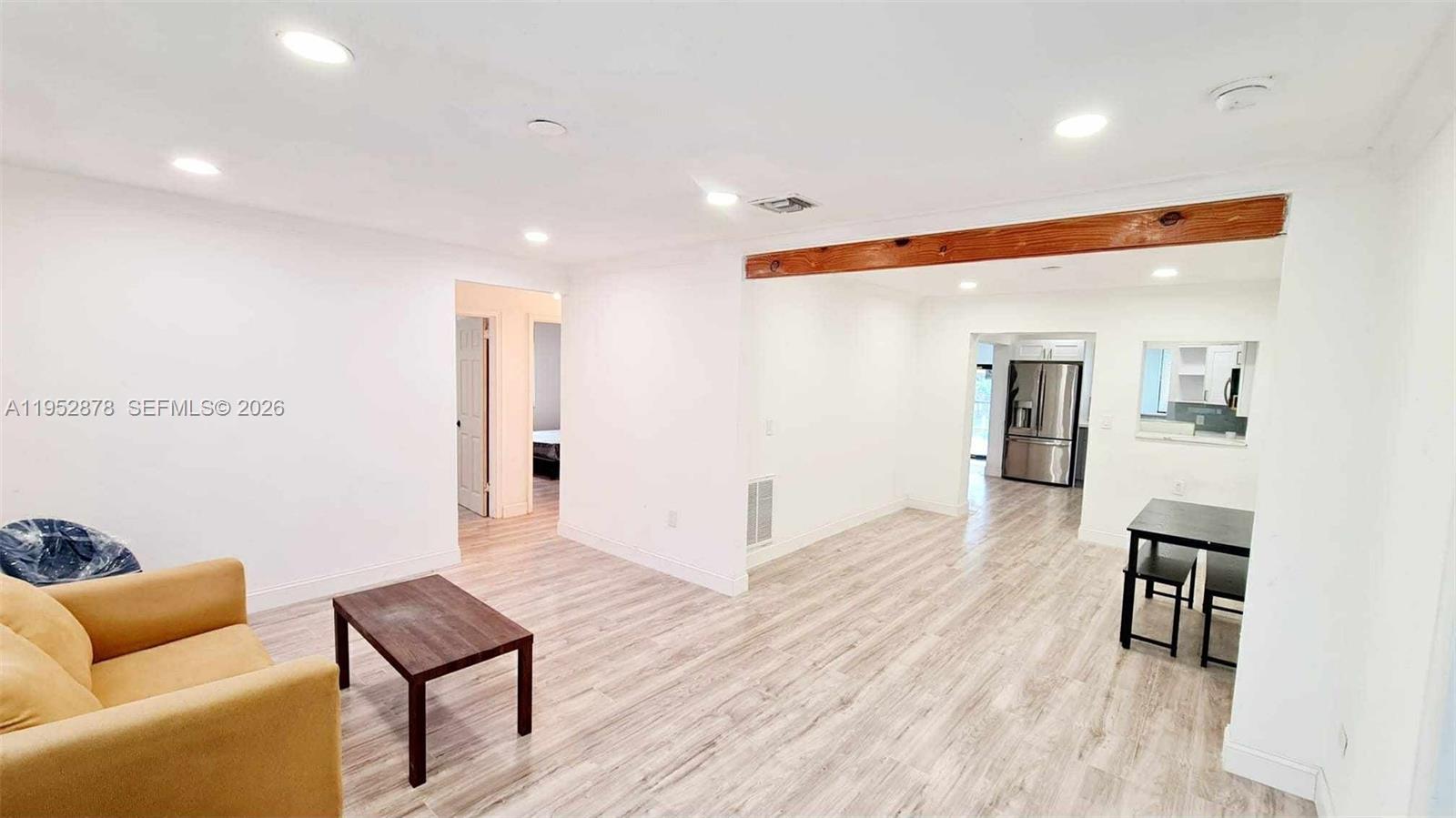 A living room with light wood-look flooring, a yellow sofa, and a wooden ceiling beam — 12040 N Miami Ave, North Miami FL 33168, NORTH MIAMI, FL