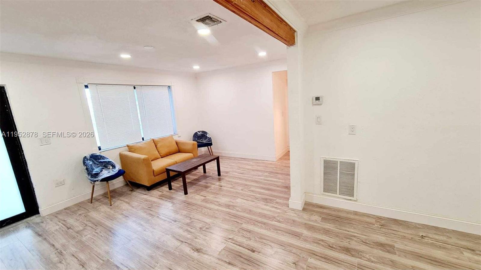 A living room features light wood-look flooring, white walls, a yellow sofa, and recessed lighting — 12040 N Miami Ave, North Miami FL 33168, NORTH MIAMI, FL