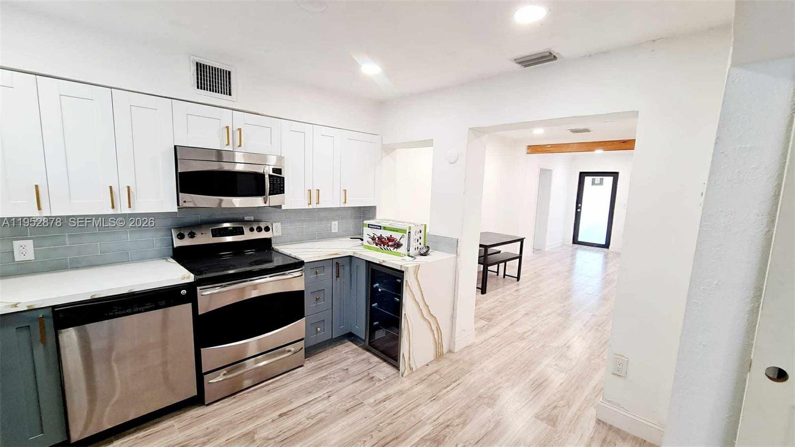 A kitchen features white upper cabinets, blue lower cabinets, stainless steel appliances, and wood-look flooring — 12040 N Miami Ave, North Miami FL 33168, NORTH MIAMI, FL
