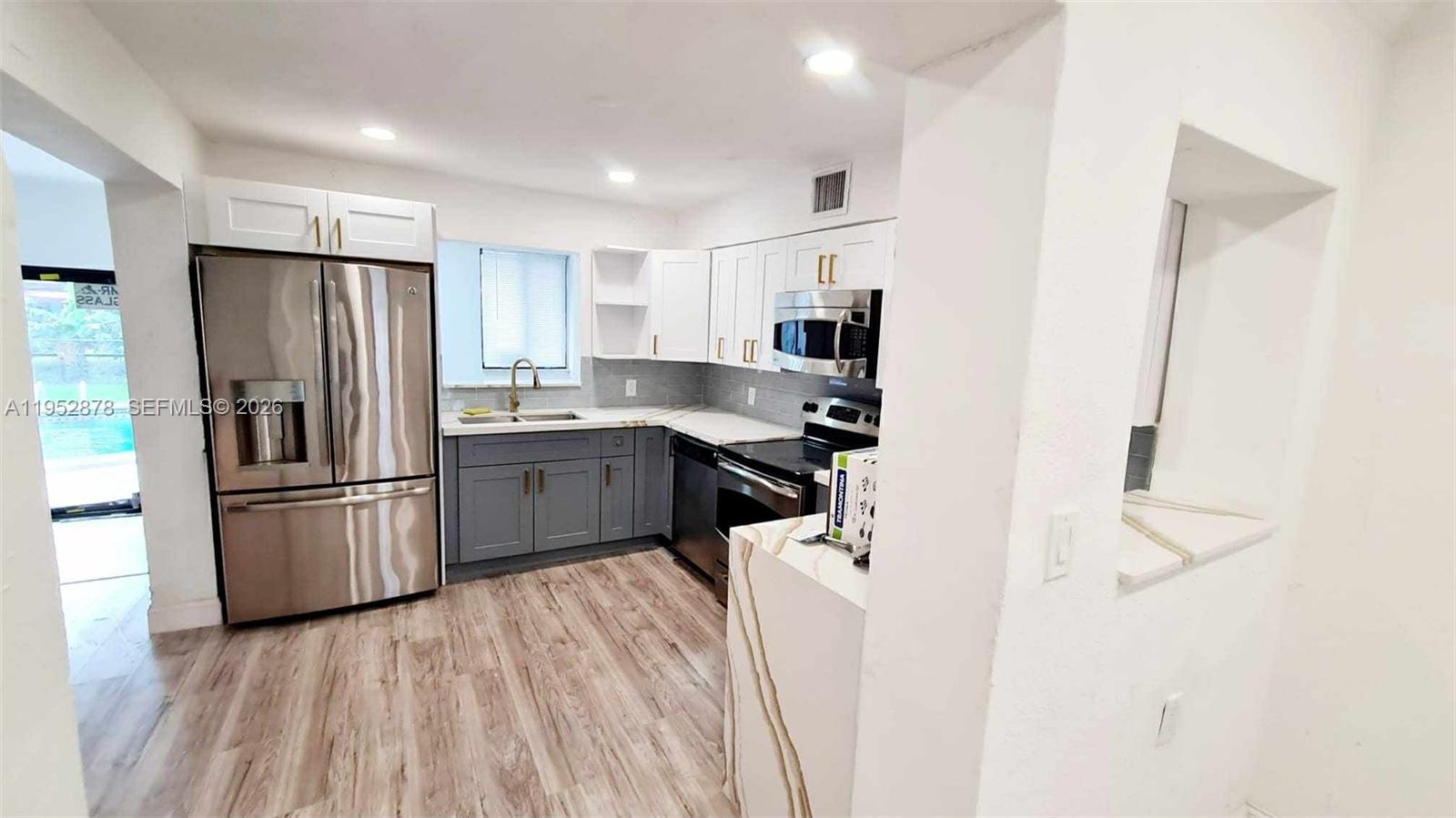 A kitchen features stainless steel appliances, gray lower cabinets, white upper cabinets, and wood-look flooring — 12040 N Miami Ave, North Miami FL 33168, NORTH MIAMI, FL