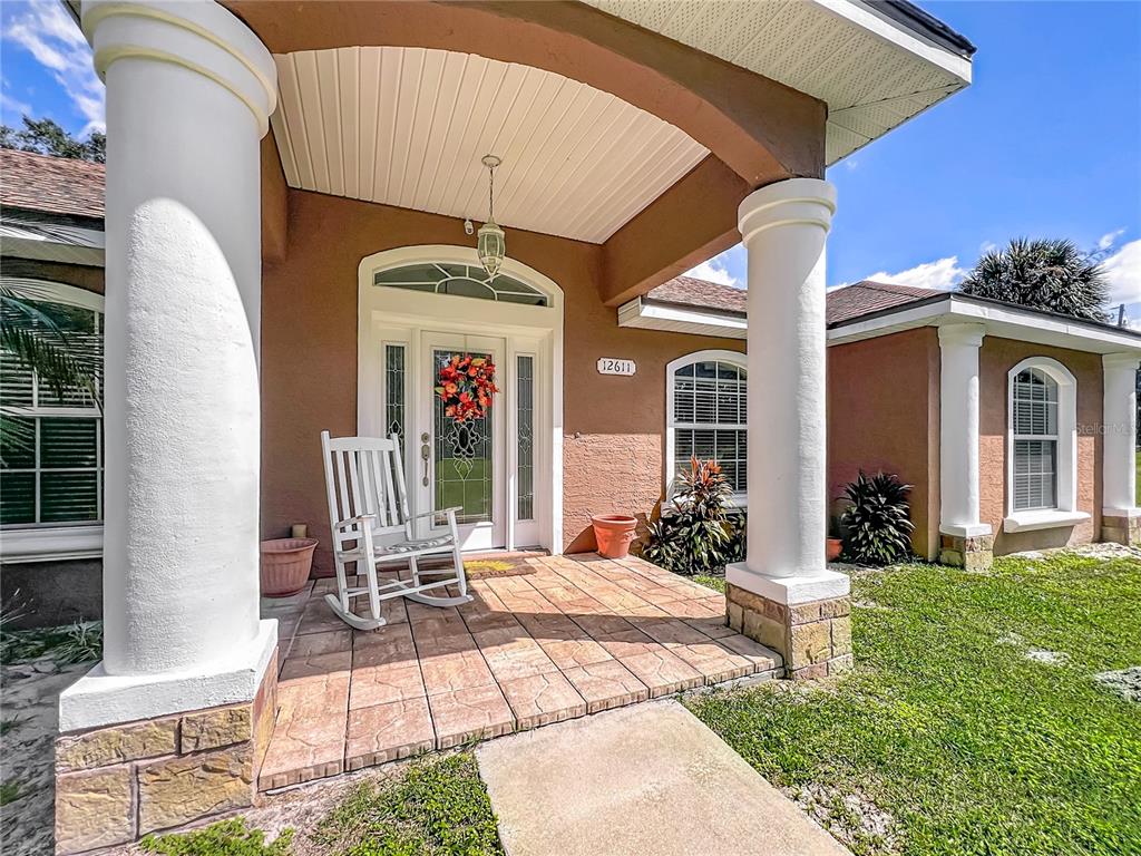 A covered front porch features a white rocking chair, columns, and a glass-paneled front door — 12611 NE 36TH AVENUE, ANTHONY, FL