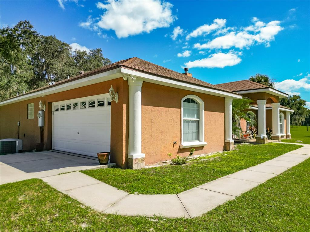 A side view of a tan stucco house with a white garage door and columns — 12611 NE 36TH AVENUE, ANTHONY, FL