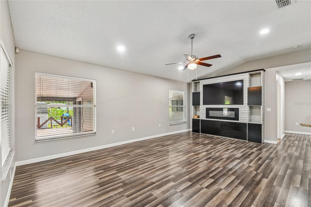 A living room features wood-look flooring, a ceiling fan, and a built-in media center — 1965 ALAMEDA DRIVE, DELTONA, FL