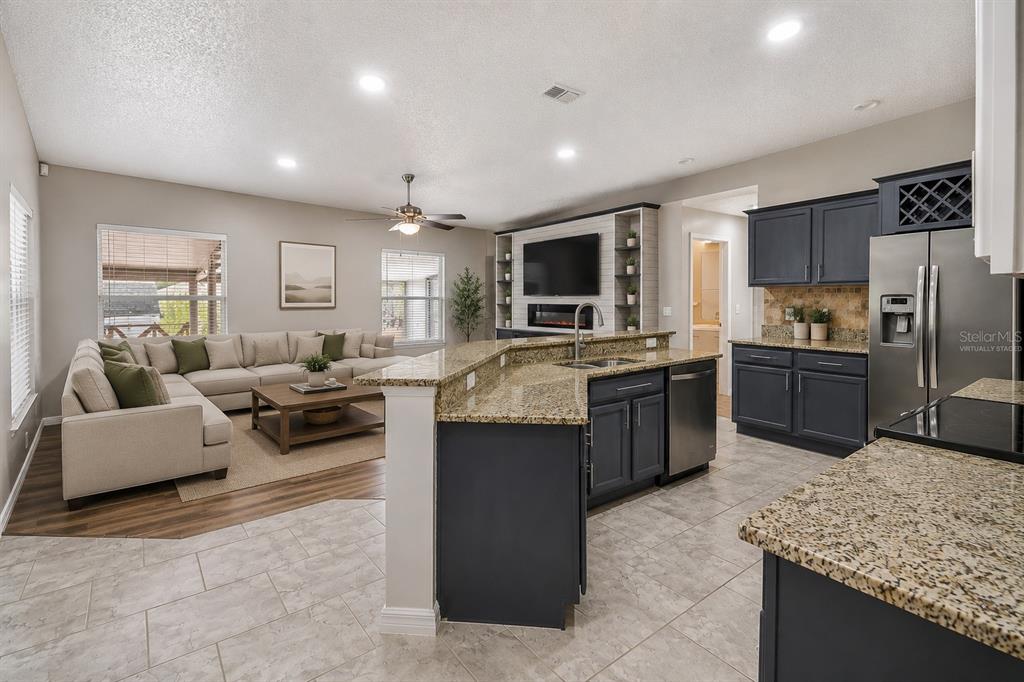 An open-concept kitchen with dark cabinets and granite countertops overlooks a living room with seating — 1965 ALAMEDA DRIVE, DELTONA, FL