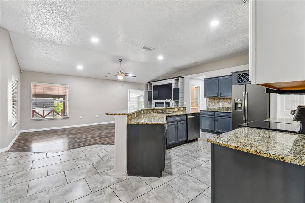 A kitchen with dark cabinets and granite countertops opens into a living area with flooring — 1965 ALAMEDA DRIVE, DELTONA, FL