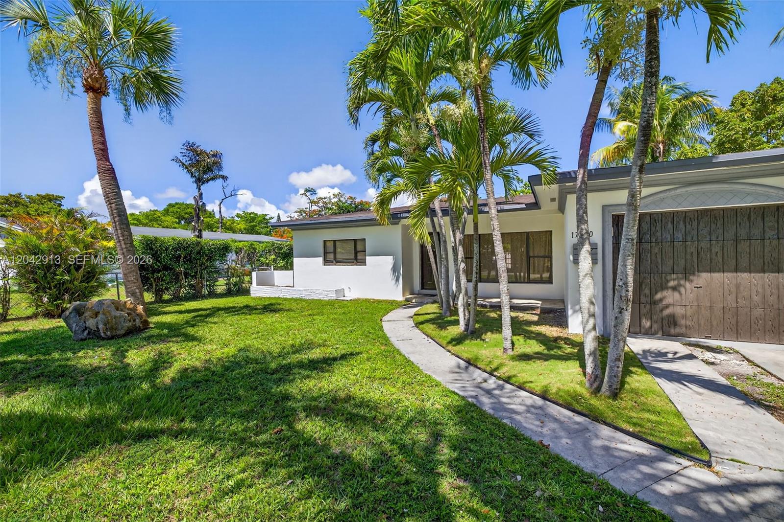 A white single-story house features a curved concrete walkway and several palm trees — NORTH MIAMI BEACH, FL