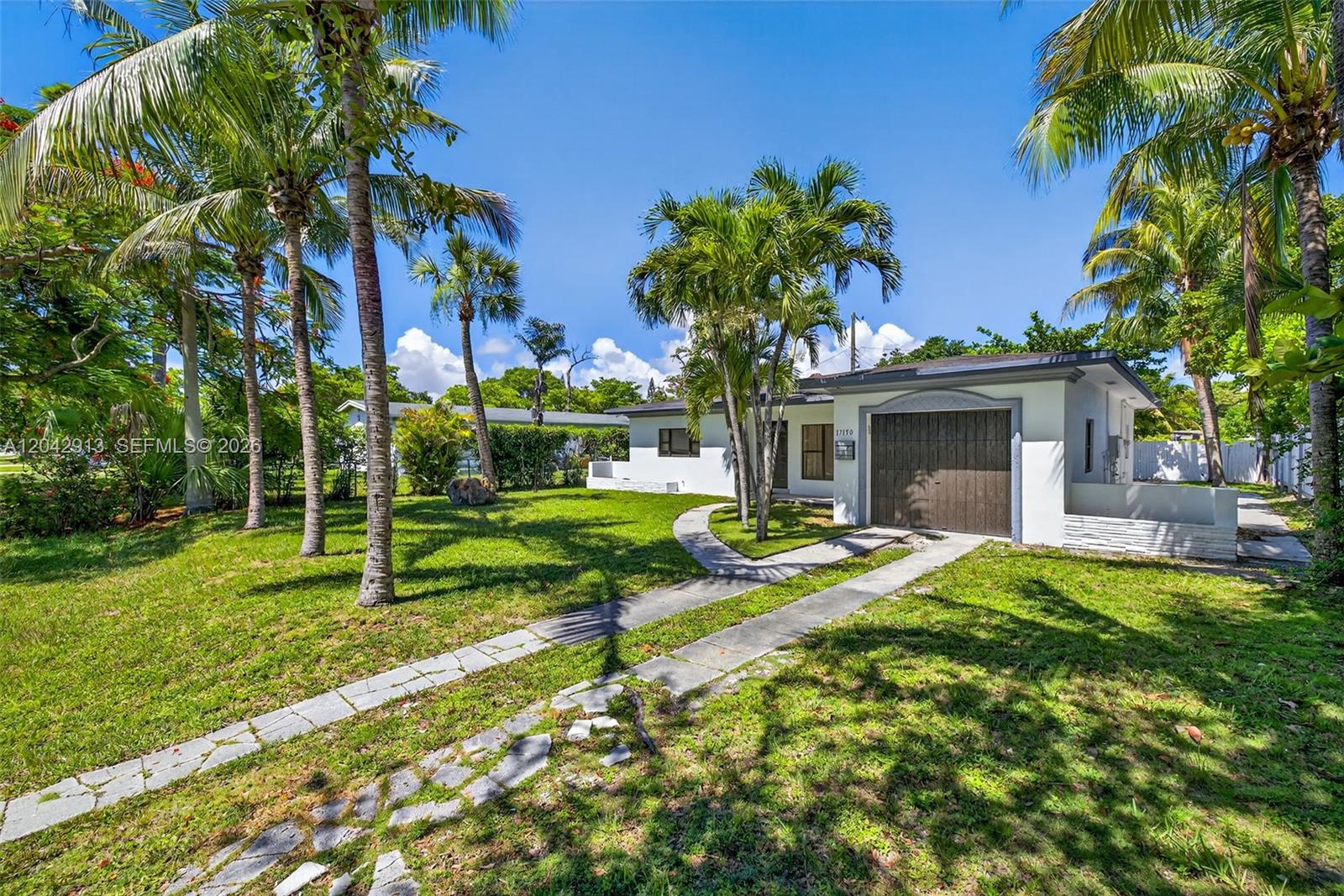 A white single-story house with a brown garage door sits on a grassy lot — NORTH MIAMI BEACH, FL