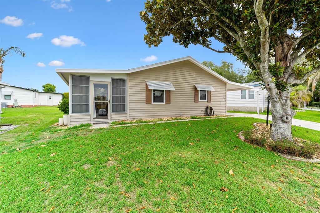 A single-story house with tan siding, a screened front porch, and a large shade tree — 1534 HILLCREST DRIVE, LADY LAKE, FL
