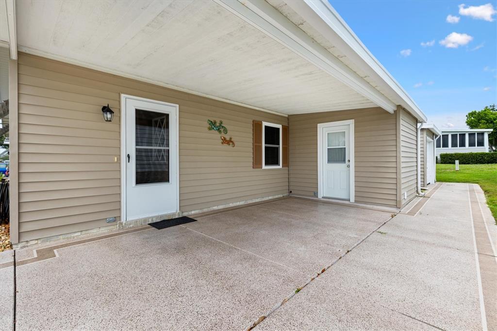 A concrete carport area features two white doors and beige horizontal siding — 1534 HILLCREST DRIVE, LADY LAKE, FL