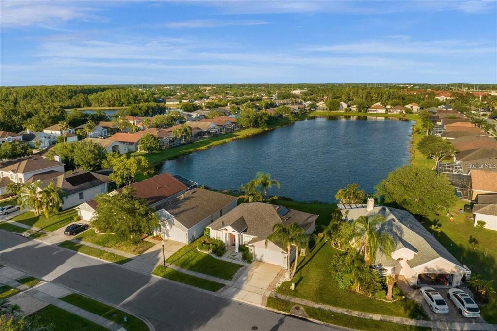 An aerial view shows suburban houses surrounding a large lake under a blue sky — 13131 LUXBURY LOOP, ORLANDO, FL