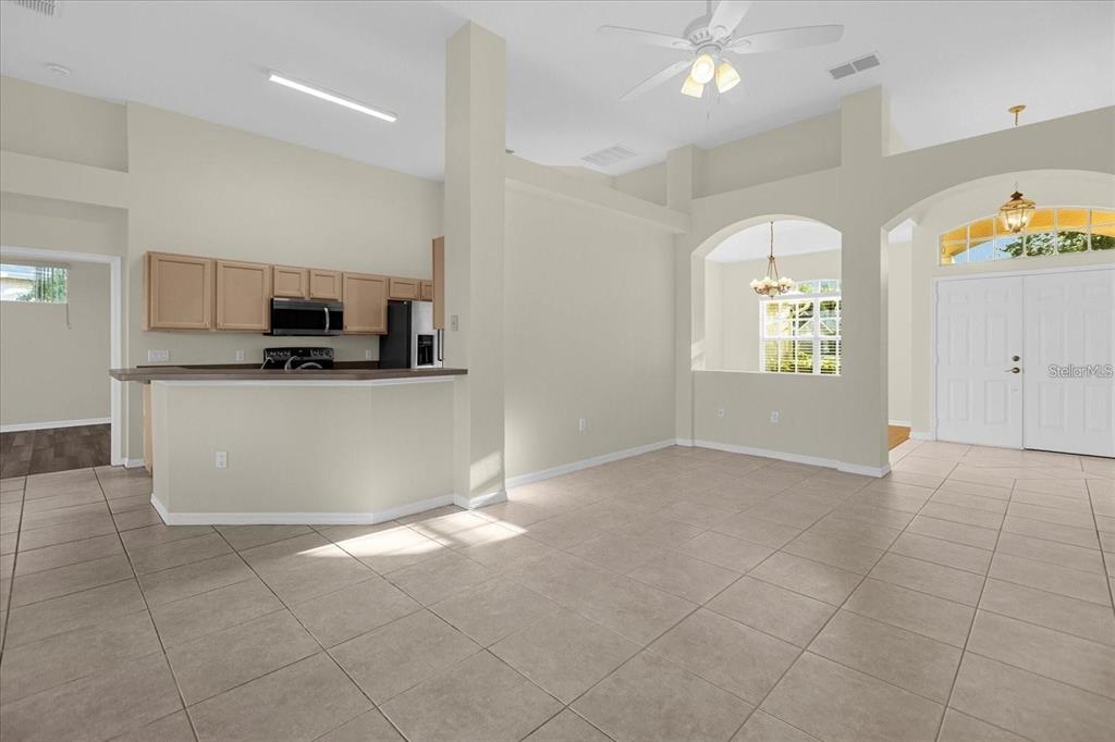 An open-concept living area features light tile flooring, a kitchen with wood cabinets, and arched entryways — 13131 LUXBURY LOOP, ORLANDO, FL