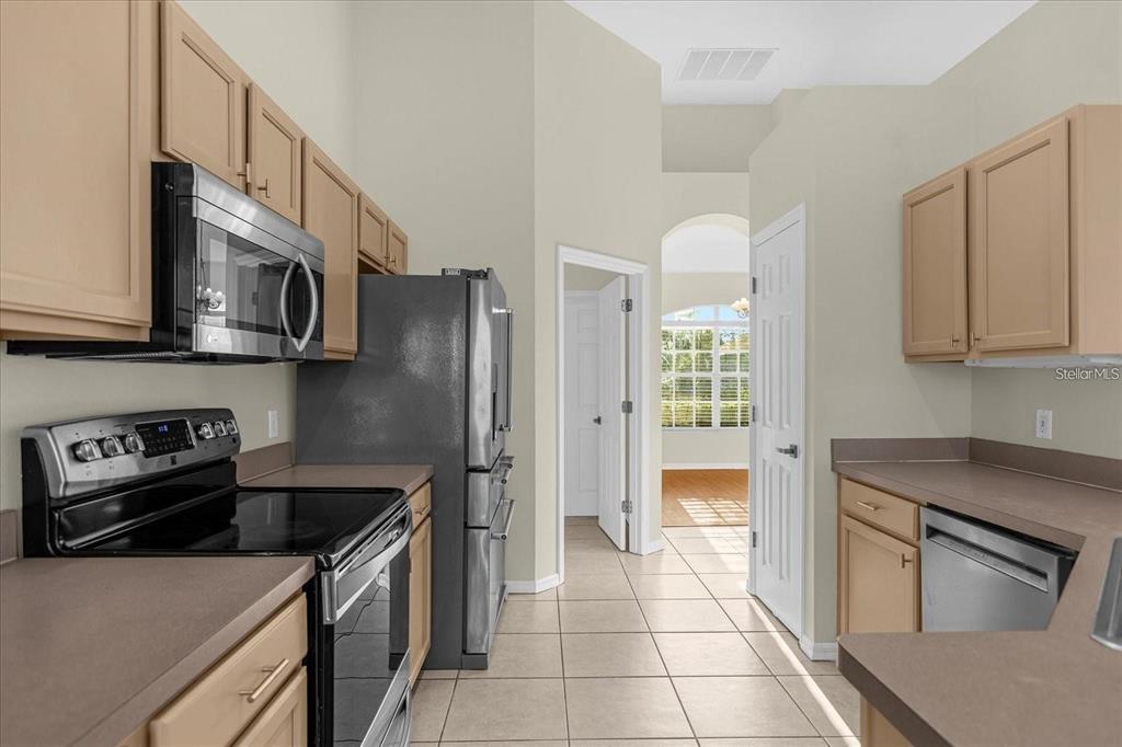 A kitchen features light wood cabinets, stainless steel appliances, and tile flooring — 13131 LUXBURY LOOP, ORLANDO, FL