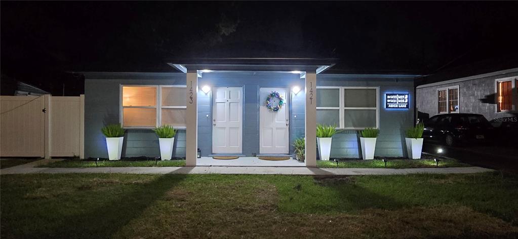 A blue duplex exterior at night features two white front doors and four potted plants — 1421, 1423, 1425, 1427 ASHER LANE, ORLANDO, FL