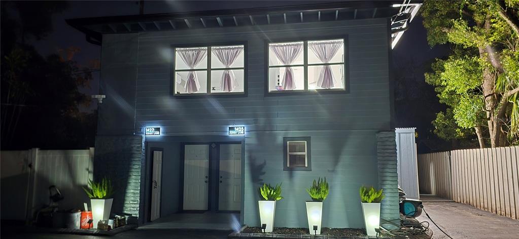A two-story blue house exterior at night with illuminated address signs and potted plants — 1421, 1423, 1425, 1427 ASHER LANE, ORLANDO, FL