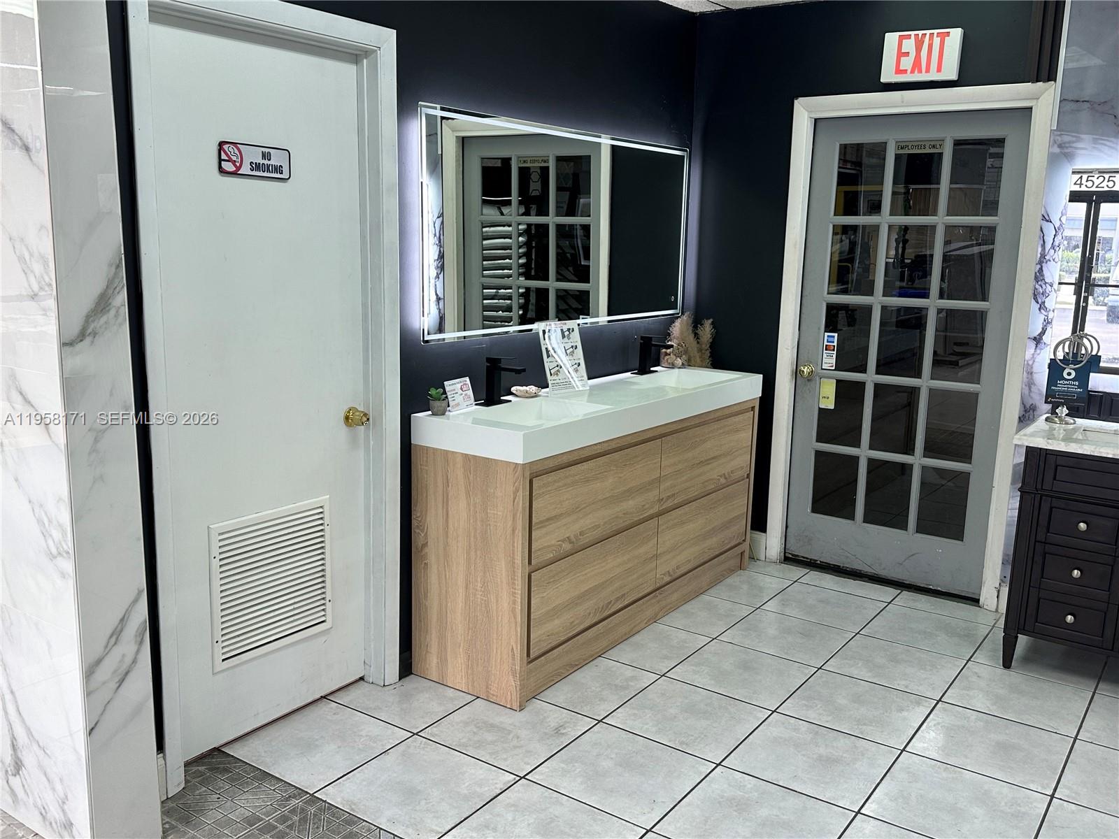 A bathroom vanity with a light wood finish sits against a black wall with mirrors — DORAL, Doral FL 33166, DORAL, FL
