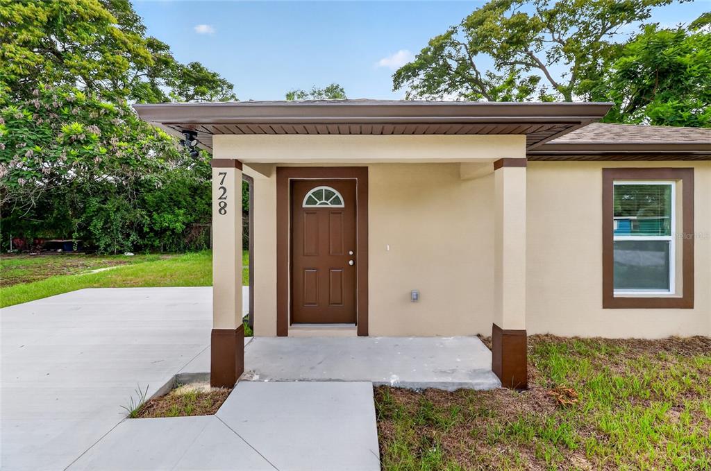 The exterior of a house features a tan facade, a brown front door, and a porch — 728 HENRY ST, AUBURNDALE, FL