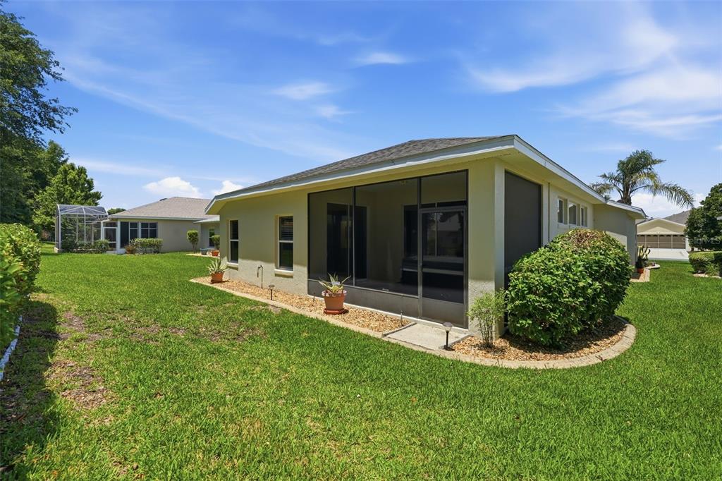 The exterior of a house features a screened-in patio, a grassy yard, and landscaping — 27144 STONEY BROOK DRIVE, LEESBURG, FL