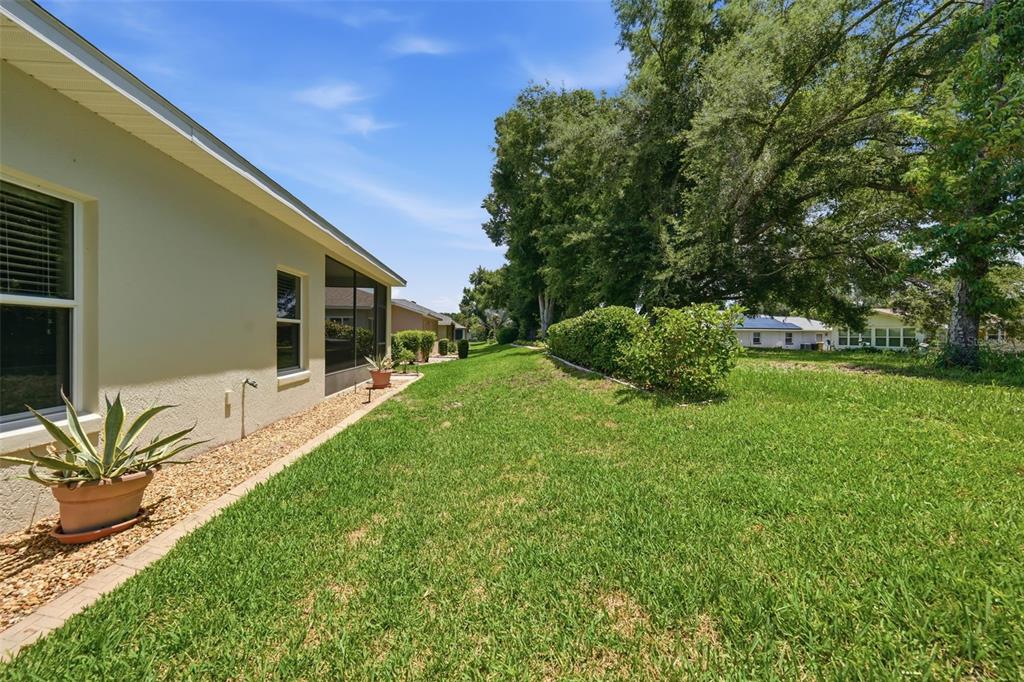 A side view of a house exterior with a grassy yard and a gravel border — 27144 STONEY BROOK DRIVE, LEESBURG, FL