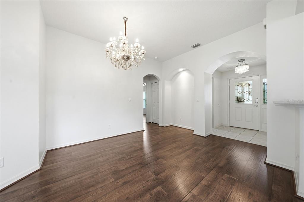 An empty room with dark wood floors, white walls, and two crystal chandeliers — 27144 STONEY BROOK DRIVE, LEESBURG, FL