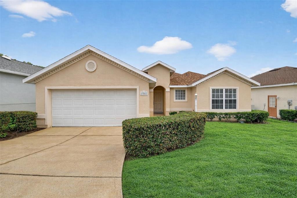 A single-story house with a beige stucco exterior, a two-car garage, and a manicured lawn — 17867 SE 115TH CIRCLE, SUMMERFIELD, FL