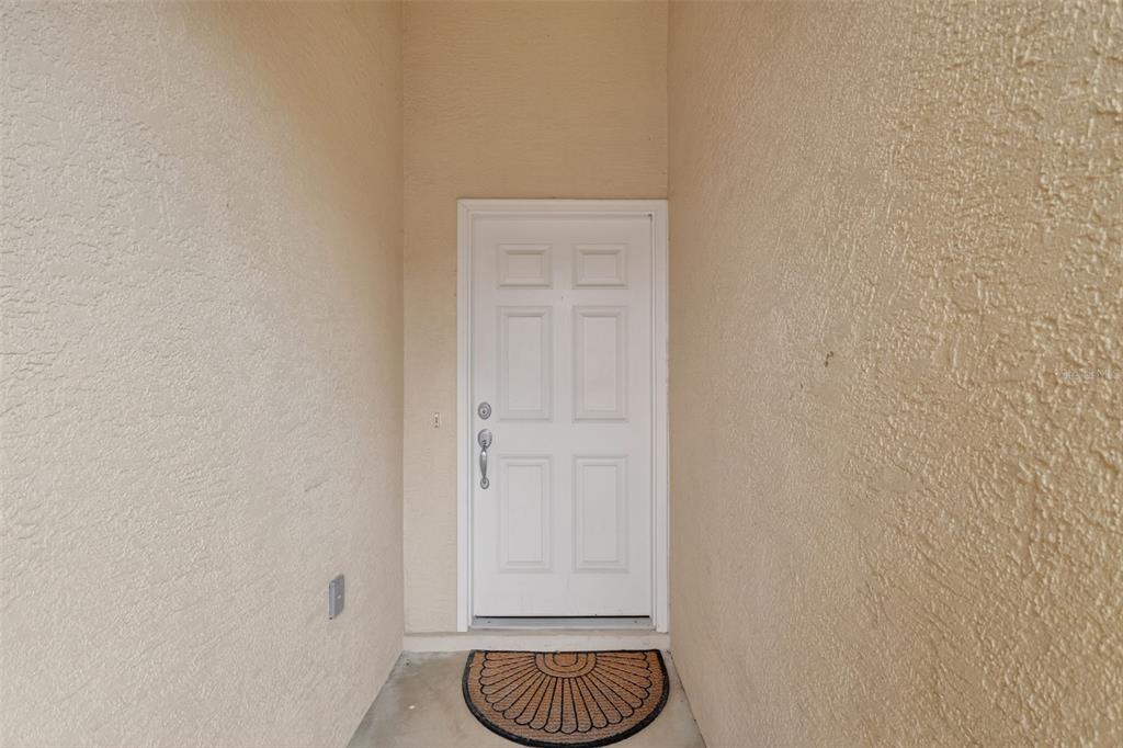 A white front door with a semi-circular doormat is set within a recessed stucco entryway — 17867 SE 115TH CIRCLE, SUMMERFIELD, FL