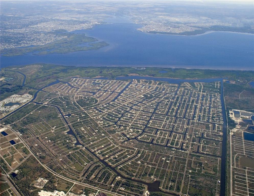 An aerial view shows a residential neighborhood with canal-front lots near a large body of water — 13470 LANSING AVENUE, PORT CHARLOTTE, FL