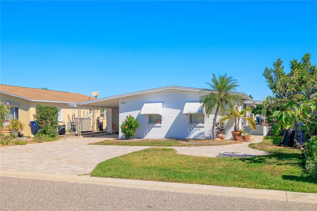 A single-story white house with a carport, paved driveway, and palm trees under a blue sky — 17611 1ST STREET E, REDINGTON SHORES, FL