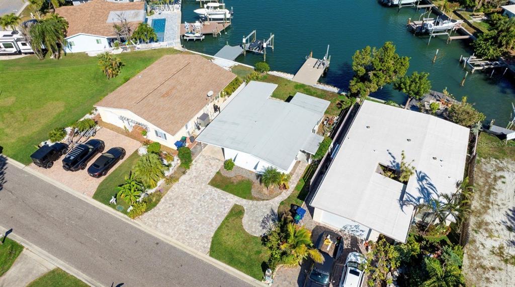 An aerial view shows three waterfront houses with paved driveways and private boat docks — 17611 1ST STREET E, REDINGTON SHORES, FL