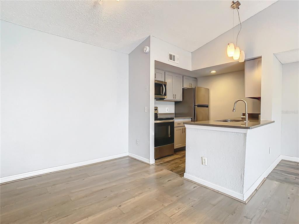 A kitchen with stainless steel appliances and light wood-look flooring opens to a dining area — 5144 CONROY ROAD UNIT 35, ORLANDO, FL