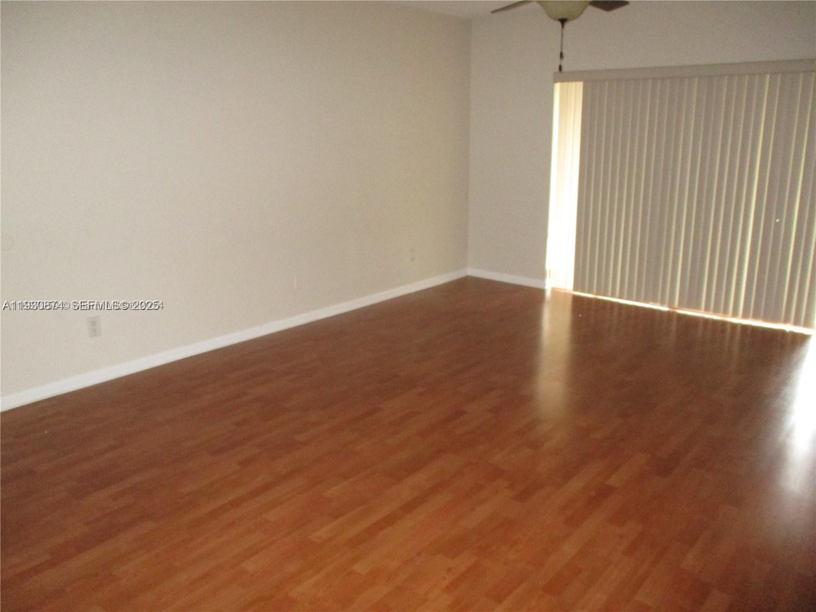 An empty room features light-colored walls, wood-look flooring, and a sliding glass door with blinds — 13726 SW 90th Ave # 26, Miami FL 33176, MIAMI, FL