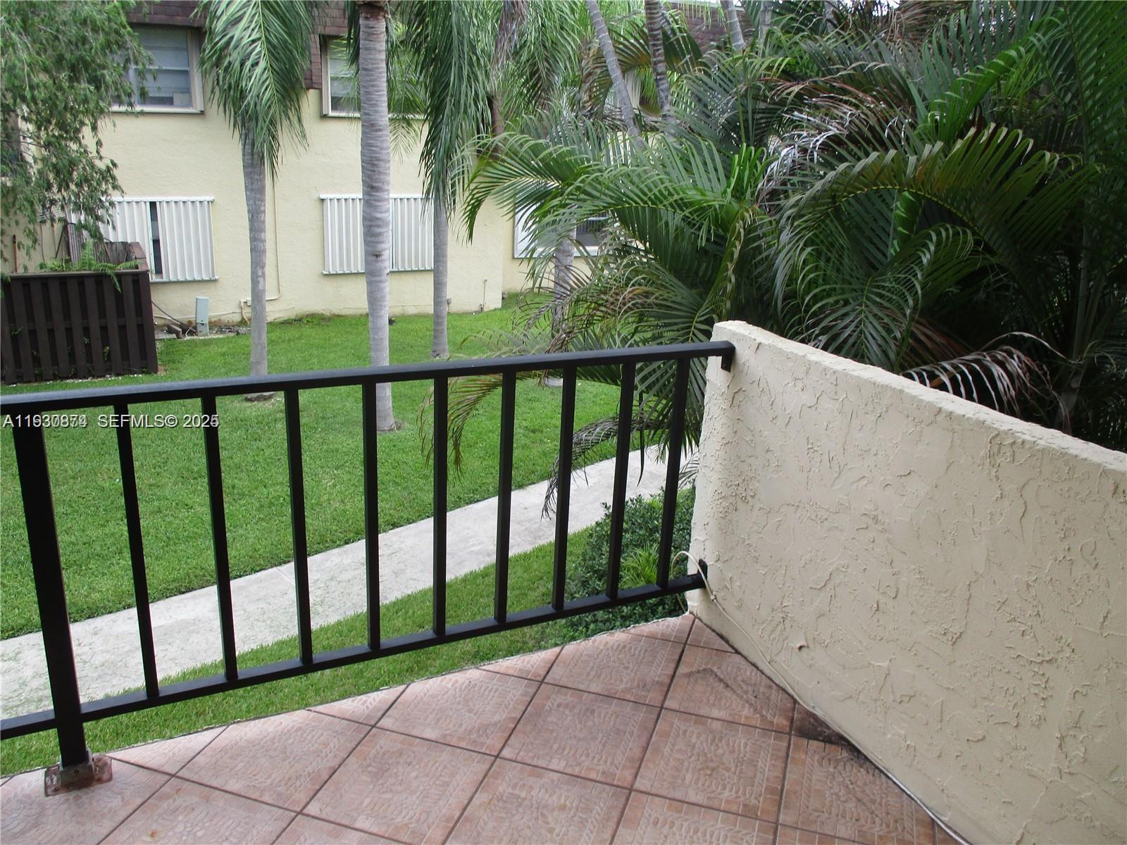 A tiled balcony with a black metal railing overlooks a grassy courtyard with palm trees — 13726 SW 90th Ave # 26, Miami FL 33176, MIAMI, FL