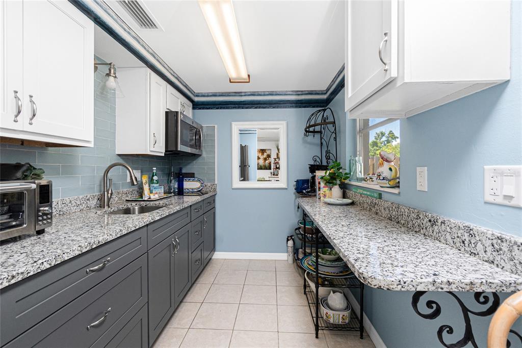 A galley kitchen features gray lower cabinets, white upper cabinets, granite countertops, and blue walls — 26 FRENCH AVENUE, ENGLEWOOD, FL