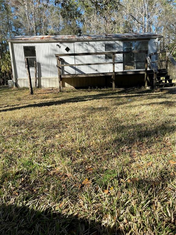 An exterior view of a weathered mobile home featuring a wooden deck and metal roof — 10379 NE HIGHWAY 314, SILVER SPRINGS, FL